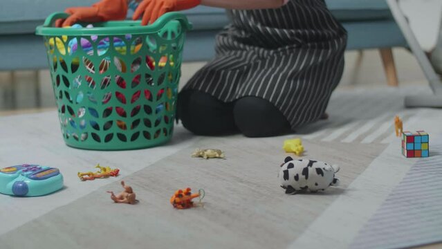 Close Up Of Female Housekeeper'S Hands Collect The Toys To The Plastic Basket In The Messy Room 
