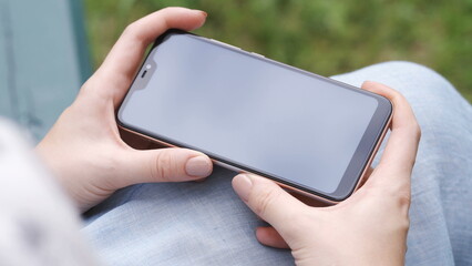 The girl holds a smartphone horizontally and watches the video on the screen. Green screen smartphone for tracking. Concept - social networking, mobile Internet, media content on a smartphone
