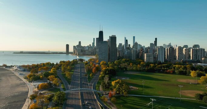 Flying backwards along the main road leading to Chicago Downtown with skyscrapers on horizon. Sunrise light with autumn multicolor trees