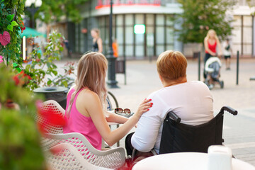 Woman with disability sitting in a wheelchair in outdoor cafe with her young daughter