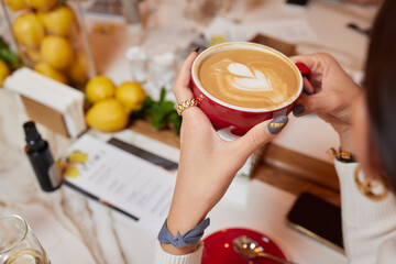 Close-up top view of unrecognizable young woman holding cup of hot latte coffee with beautiful...