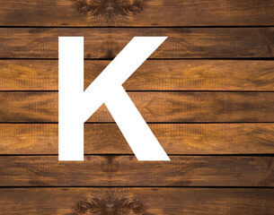 Alphabet letter K in white hole on wood background