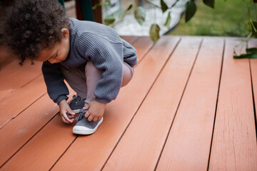 Biracial toddler putting on shoe - obrazy, fototapety, plakaty