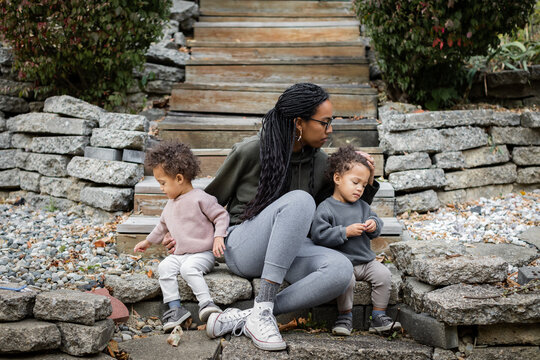 Black mom sitting with toddler twins on steps in backyard in fall 