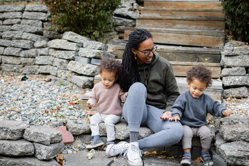 Biracial mom sitting with twins on steps in backyard in fall