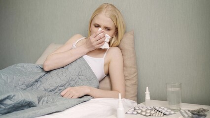 .Young sick woman sneezing at home at night on the couch. Girl runny nose and holding tissue, flu symptoms