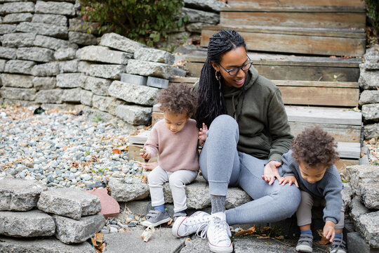 Biracial mom sitting with twins on steps in backyard in fall