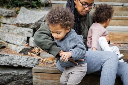 Black mother helping biracial son down the stairs in backyard in fall 