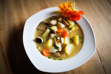 herbstliche Pilzsuppe mit Kapuzinerkresseblüten und Kartoffeln in einem weißen Suppenteller auf einem Holztisch