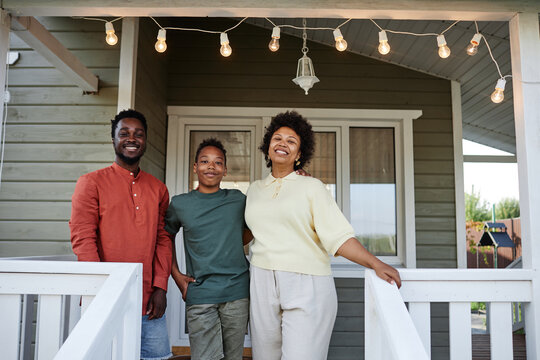Portrait of happy black family standing on porch of new house and smiling at camera, copy space