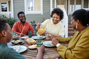 Fototapeta na wymiar Portrait of smiling black woman pouring lemonade drinks to glass during family gathering outdoors