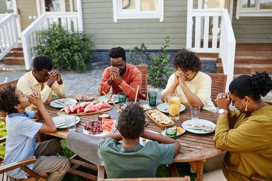 High angle view at group of African American people praying at picnic table outdoors during family gathering