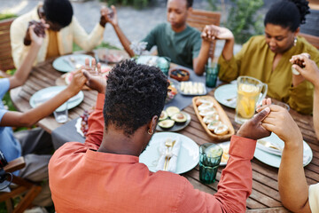High angle view at African American family saying grace at table outdoors and holding hands during gathering
