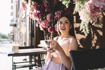 Surprised millennial woman text messaging via mobile phone in street cafe