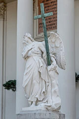 Statue of sensual Renaissance Era angel with wings and big cross in front of Saint Karl Cathedral...