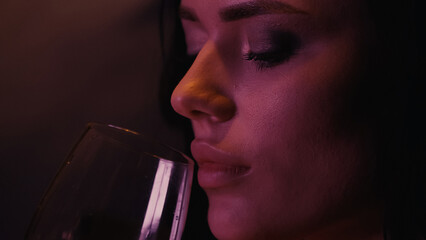 Young woman holding glass on black background with lighting.