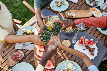 Top view at group of African American people clinking glasses over table with delicious food outdoors