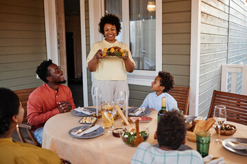 Portrait of senior black woman bringing food to table while enjoying family gathering outdoors