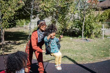 Fototapeta premium Black mom pushes toddler girl on swing in park in fall 