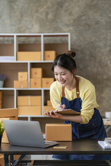 Online delivery concept, woman smiling at the box while checking the order. Freelancers or salespeople inspecting production packaging. SMEs work on boxes at home.