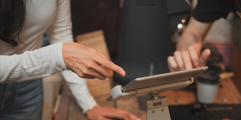 close up of Female worker's hands showing gesture an explaining with menu on tablet in coffee shop bar counter to customer. digital tablet with blank screen. 