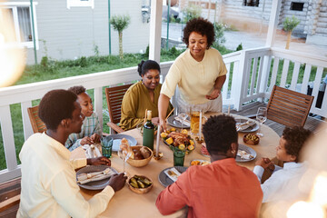 African American family at dinner table outdoors with smiling woman bringing homemade dishes