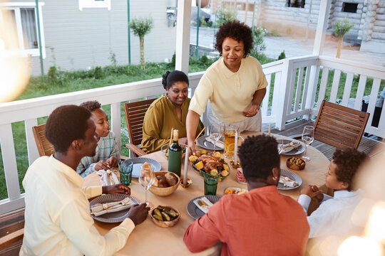 African American Family At Dinner Table Outdoors With Smiling Woman Bringing Homemade Dishes