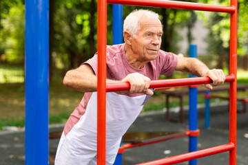 Obraz premium Elderly man doing fitness on sports ground equipment in park