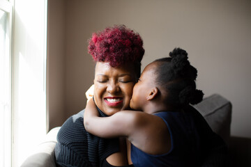 African American girl giving her mother a hug and kiss on cheek - obrazy, fototapety, plakaty