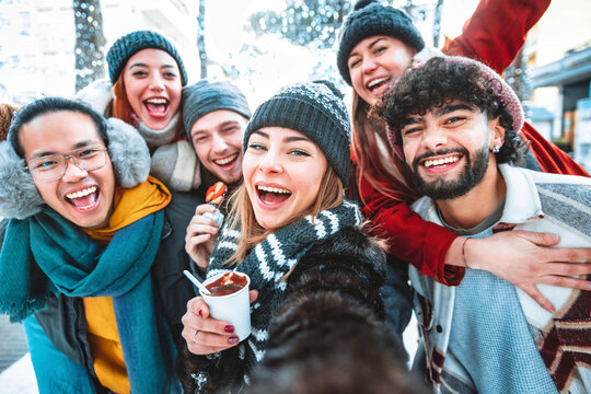 Multicultural friends wearing winter clothes taking selfie with smart mobile phone outdoors - Happy young people celebrating new year event party together - Friendship and winter holidays concept