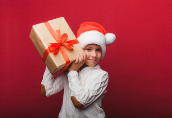 Cute little boy in a Santa Claus hat holding a gift box on a red background. a child with a New Year's gift for Christmas. new year