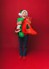 a boy in a knitted red sweater and a Santa Claus hat holds a Christmas boot for gifts. Cute baby is waiting for Christmas and a new kind. insulation on a red background.