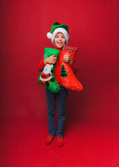 a boy in a knitted red sweater and a Santa Claus hat holds a Christmas boot for gifts. Cute baby is waiting for Christmas and a new kind. insulation on a red background.