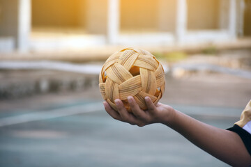 Sepak takraw ball, southeast asian countries traditional sport, holding in hand of young asian female sepak takraw player in front of the net before throwing it to another player to kick over the net.