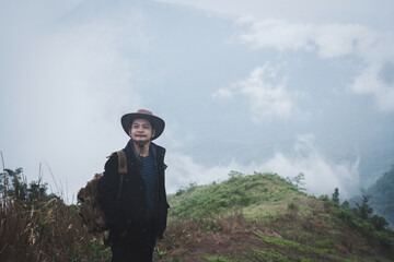 Freedom traveler man in hat carrying a backpack stands at the top of a mountain on a foggy day.Adventure travel and success concept
