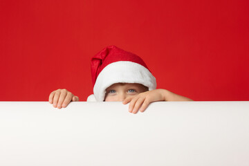 Sly look of little boy in red cap during the game, hiding behind white banner. Cute child in funny hat looks out from behind banner