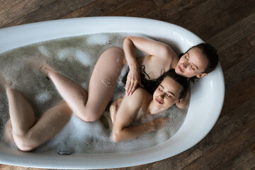 top view of sexy lesbians with closed eyes taking bubble bath at home.