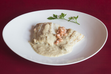 An elegant presentation of a serving of cod with green sauce and prawns garnished with a parsley leaf on a red studio background. Easy and healthy recipes.
