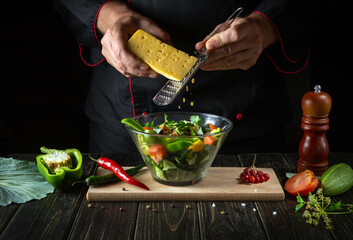 The cook prepares vegetarian food from fresh vegetables. Menu concept for hotel on dark background. Adding cheese to a salad.