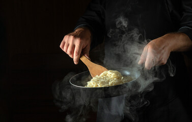 Cooking spaghetti in a frying pan in the hands of a chef. Space for advertising on a black background