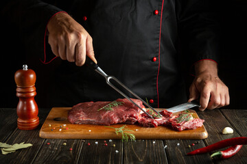 The chef prepares raw meat on a kitchen cutting board. Idea for a hotel menu on a dark background