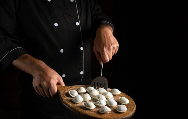 The chef cooks dumplings in the hotel kitchen. Free space for advertising. The concept of a delicious lunch on a black background.