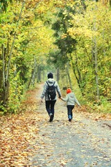 Fototapeta premium A couple of a woman and a child walking in the park autumn fall road