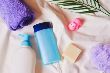 Obraz na płótnie Canvas Baby care cosmetic products flat lay photography. Purple towel, liquid soap, shampoo bottle, soap bar, bath toy hippo and sponge