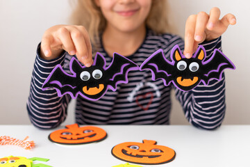 little girl holding Halloween bats decorations with spooky face. Holiday activities for kids. closeup