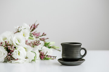 Fototapeta na wymiar Black ceramic cup with coffee on table and bouquet of flowers.