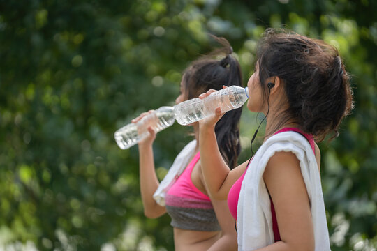 Two female friends relax and drink water after running in a city park