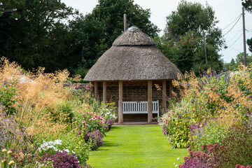 Fototapeta na wymiar pretty borders in an English garden leading down to a thatched gazebo