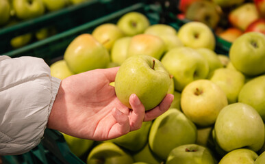 Close-up, an apple in a woman's hand, a selection of fruits in a supermarket.