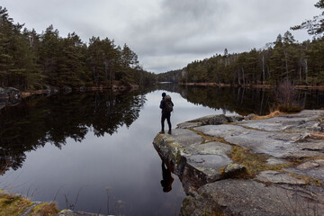 A caucasian man hiker standing on a rock over looking a  lake in the forest watching reflections in the water with dramatic clouds in the sky.